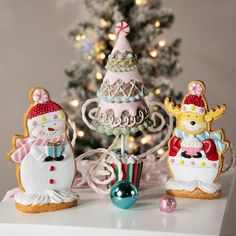 three decorated christmas cookies sitting on top of a white table next to a christmas tree