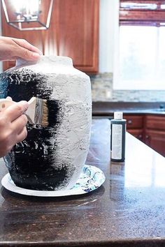 someone is decorating a black and white cake with icing on the counter top