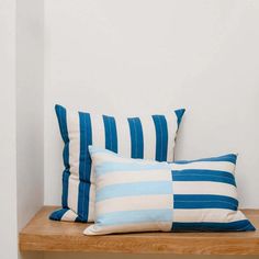 two blue and white striped pillows sitting on a wooden shelf in front of a white wall