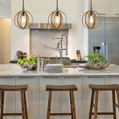 a kitchen island with three stools in front of it and lights hanging from the ceiling