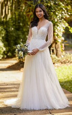 a woman in a wedding dress standing on a path with trees and bushes behind her