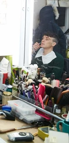 a man sitting at a desk in front of a mirror with lots of clutter on it