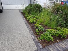 a car parked in front of a house next to a flower bed and shrubbery