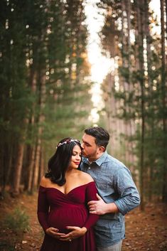 a pregnant couple standing in the woods with their arms around each other and looking into one another's eyes