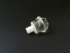 a clear glass knob with a white plastic top on a black surface in front of a black background