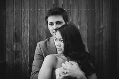 a man and woman hugging each other in front of a wooden wall, black and white photo