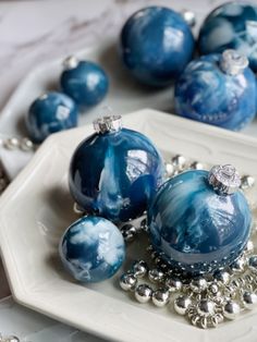 some blue ornaments are sitting on a white plate with silver balls and chains around them