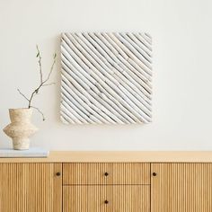 a vase sitting on top of a wooden dresser next to a wall mounted art piece