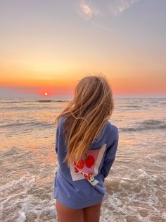 a woman is standing in the water at the beach with her back to the camera