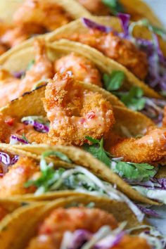 several tacos with shrimp and coleslaw are lined up on a table top