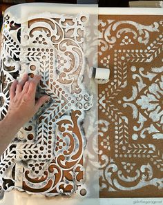 a person is painting an intricate design on a piece of cardboard with white paint and brown paper