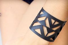 a woman's black leather bracelet with cut out geometric designs on it, sitting next to her legs