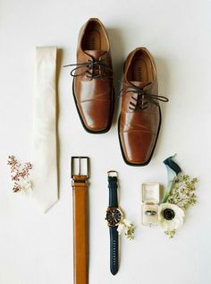 a pair of shoes, watch and tie laid out on a white surface with flowers