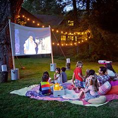 a group of people sitting on top of a blanket in front of a movie screen