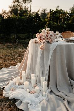 a table with candles and flowers on it in the middle of an open field at sunset