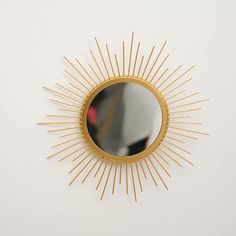 a gold sunburst mirror on a white wall with a red object in the background