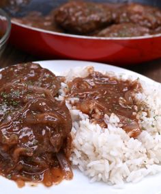 a white plate topped with rice and meat covered in gravy on top of a wooden table