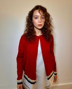 a woman standing in front of a wall wearing a red cardigan and white top