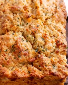 a loaf of bread with cheese and herbs on it sitting on a wooden table top