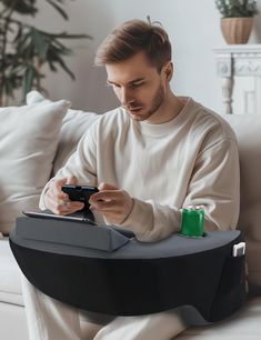 a man sitting on a couch looking at his cell phone while holding a game controller