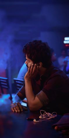 a man sitting at a table talking on a cell phone while holding his hand to his ear