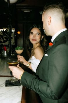 a man and woman standing next to each other at a bar with drinks in front of them