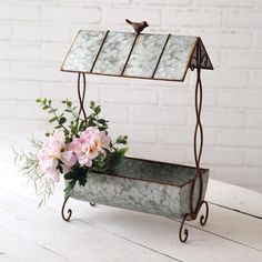 a metal planter with flowers in it sitting on a white wooden table next to a brick wall