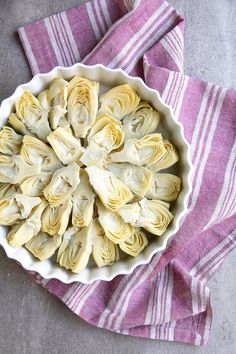 a white bowl filled with artichokes on top of a purple and white towel