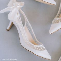 white wedding shoes with bows and pearls on the heel are shown in this photograph,