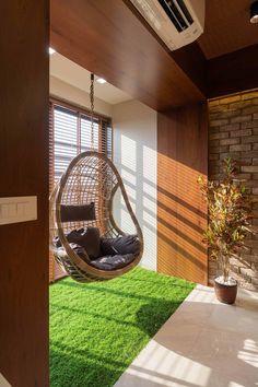 a hanging chair in the middle of a room with grass on the floor and windows