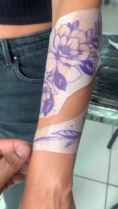 a woman is holding her arm with purple flowers on it and tape around the wrist