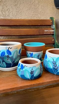 four blue and white bowls sitting on top of a wooden table next to a bench