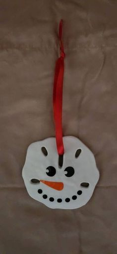 a paper snowman ornament hanging from a red ribbon on a brown sheet