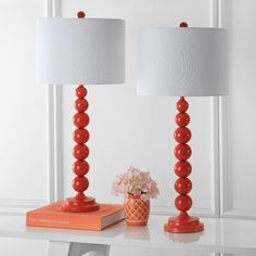 two orange lamps sitting on top of a white table next to a vase with flowers