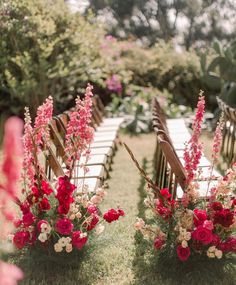 two rows of wooden chairs with red and white flowers on them sitting in the grass