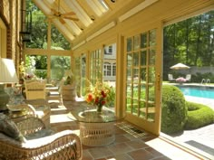 the inside of a sun room with wicker furniture and large windows overlooking a pool