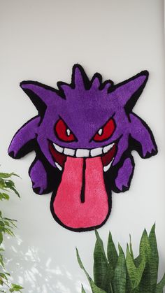 a purple monster head hanging on the wall next to a potted plant and green plants