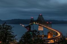 a bridge that is going over the water at night with lights shining on it's sides