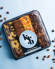 an assortment of cookies and chocolates in a plastic container on a blue surface with scattered nuts