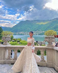 a woman in a wedding dress stands on a balcony overlooking the water and mountains with her arms around her waist