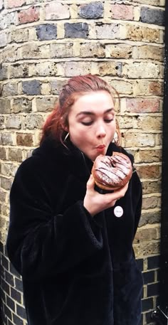 a woman eating a donut in front of a brick wall