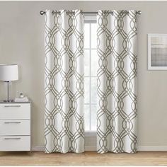 the curtains are hanging in front of a window with an intricate design on it, along with a white dresser and side table