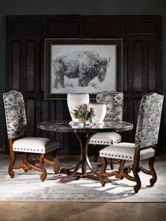 a dining room table with two chairs and a cow painting on the wall behind it