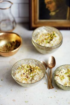 three glass bowls filled with rice and nuts next to two spoons on a table