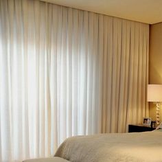 a white bed sitting under a window next to a lamp