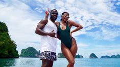 a man and woman standing on the back of a boat in front of an island