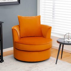 an orange chair sitting in front of a window next to a table with a lamp on it