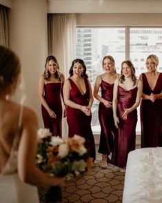 a group of women standing next to each other in front of a window holding bouquets