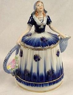 a blue and white teapot with a woman sitting on top