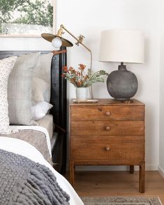 a bed room with a neatly made bed and a night stand next to the window